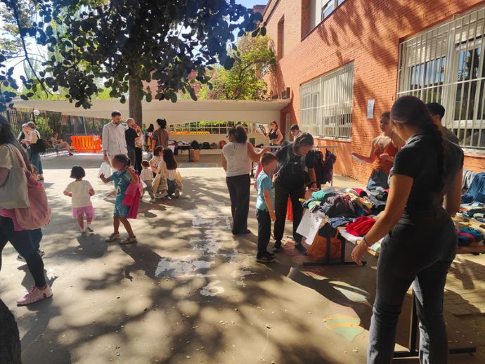 Personas asistiendo al mercadillo de ropa en el patio del colegio