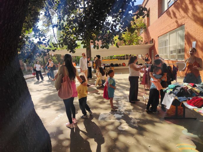 Personas y alumnado en el patio del colegio participando en el mercadillo de ropa